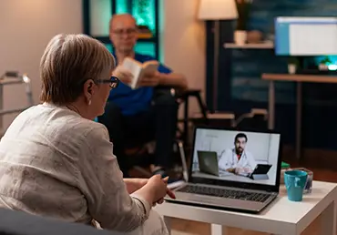 older patient using telemedicine on video call conference while sitting on couch at home