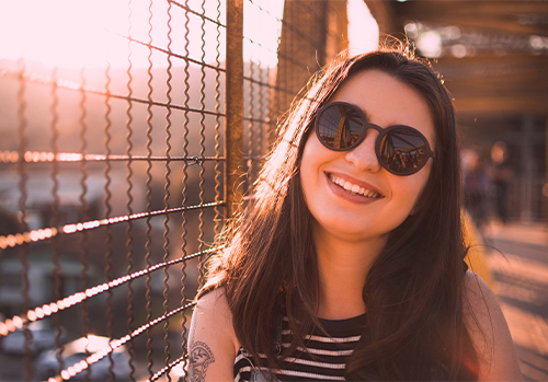 Smiling woman in sunglasses enjoying a sunset, symbolizing calm and healthy lifestyle habits for diabetic individuals.