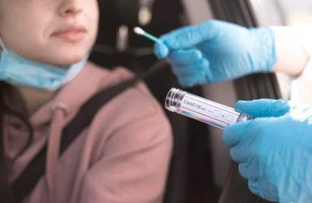 A patient sitting in her car is tested for coronavirus as part of the HHS's new state testing plans.