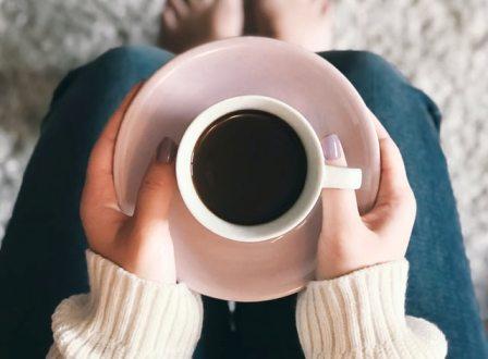 Someone holds a saucer and mug filled with black coffee that will help her take a coffee nap to make her feel more energized. 