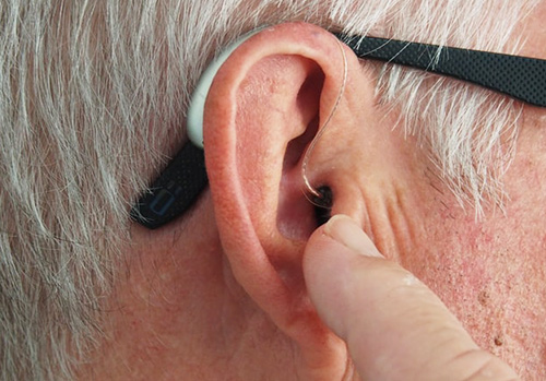 Man uses a finger to adjust his hearing aid.