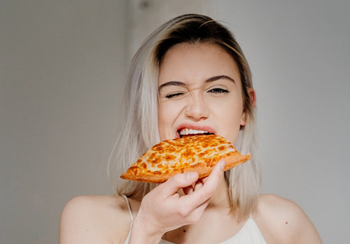 Woman takes a bite out of a piece of pizza.