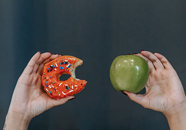 A person compares a donut vs an apple as a satiety index of common foods concept