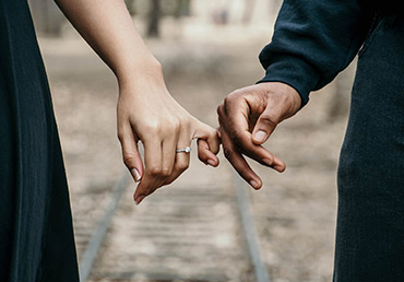 An engaged couple hold each other's pinky fingers.