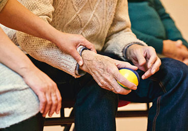 An elderly person sits with a stress ball in hand.