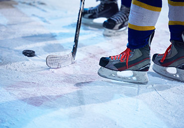 Two hockey players in skates, a hockey stick and a puck are seen on the ice.