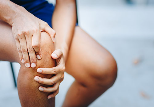 A person clutches their knee joint in pain.