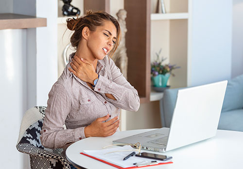 young businesswoman suffering from neckache massaging her neck while sitting at her working place