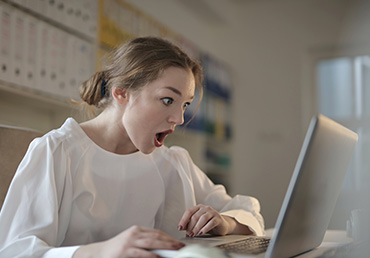 A young woman is shocked while reading her laptop.