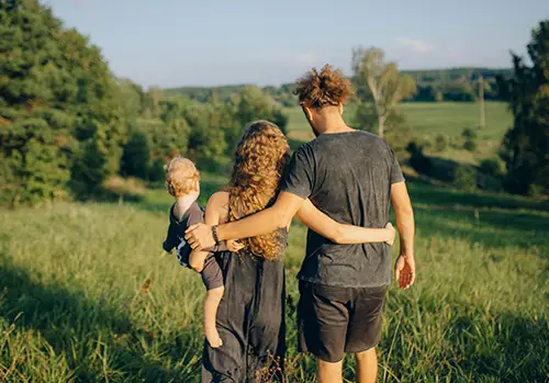 A young family walks together in a grassy field.