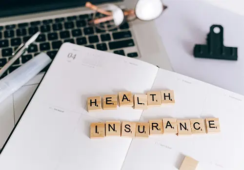 Upon a desk, tiled letters spell out health insurance.