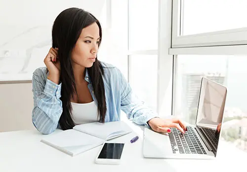 A young woman looks curiously at her laptop screen.