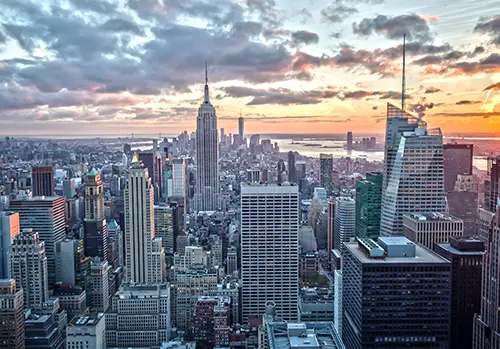 The Empire State building is photographed with its surrounding buildings at sunset.