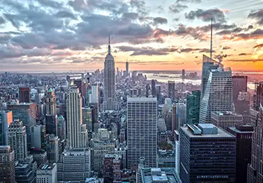 The Empire State building is photographed with its surrounding buildings at sunset.