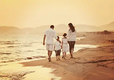 A family walks on a beach at sunset..