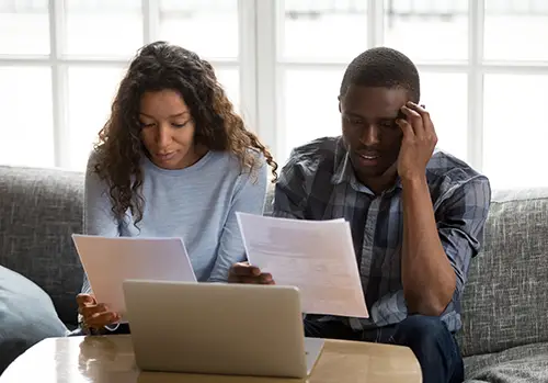 Young man and woman sit at coffee table and look over insurance plans intently.