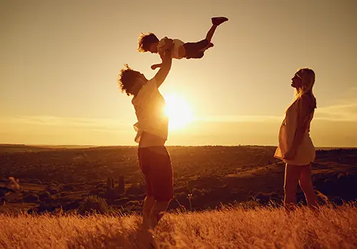 A father, mother, and child play together at sunset.