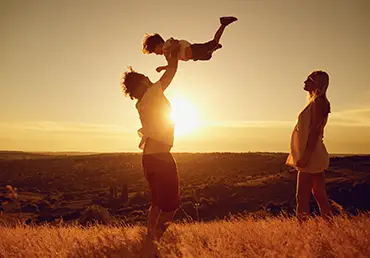 A husband, wife, and their child play together at sunset.