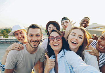 A diverse group of friends smiling and taking a selfie together on a rooftop during the day, conveying connection and emotional well‑being.