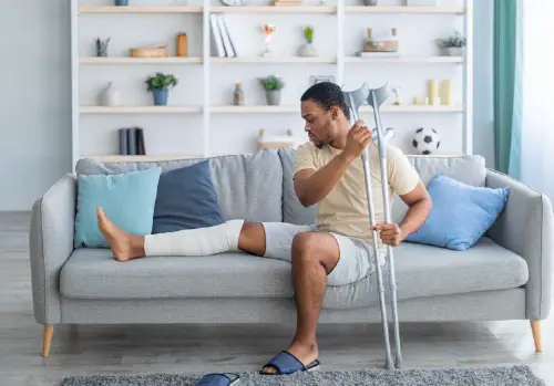 accident insurance man with crutches and broken leg sitting on couch large image