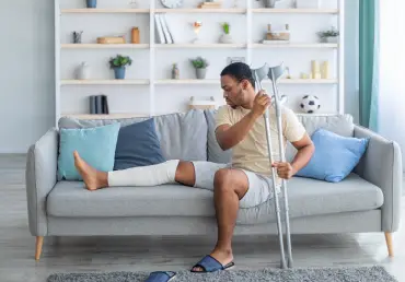 accident insurance man with crutches and broken leg sitting on couch thumbnail image