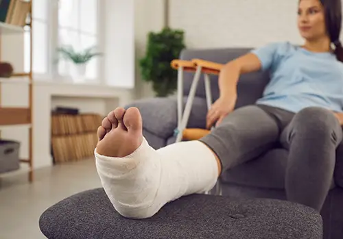 A woman sits on a couch with a foot injury.