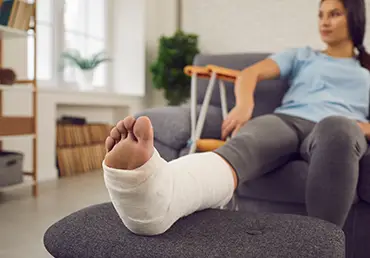A woman sits on a couch with a foot injury.