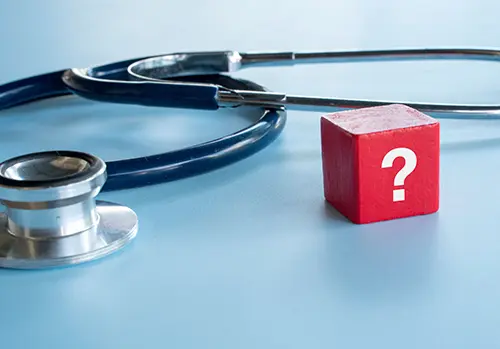 A red block with a white question mark standing next to a medical stethoscope on a blue background symbolizing medical uncertainty.