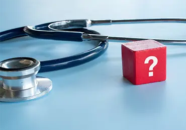 A red block with a white question mark standing next to a medical stethoscope on a blue background symbolizing medical uncertainty.